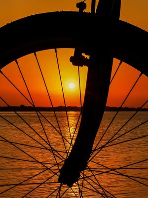 PÔR DO SOL ENTRE AROS DE UMA BICICLETA