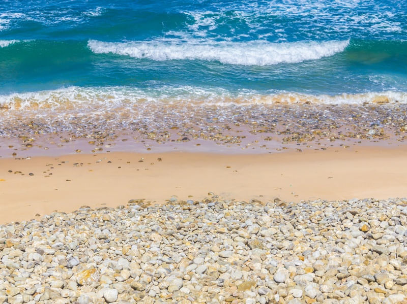 PRAIA COM PEDRAS, AREIA E ONDAS