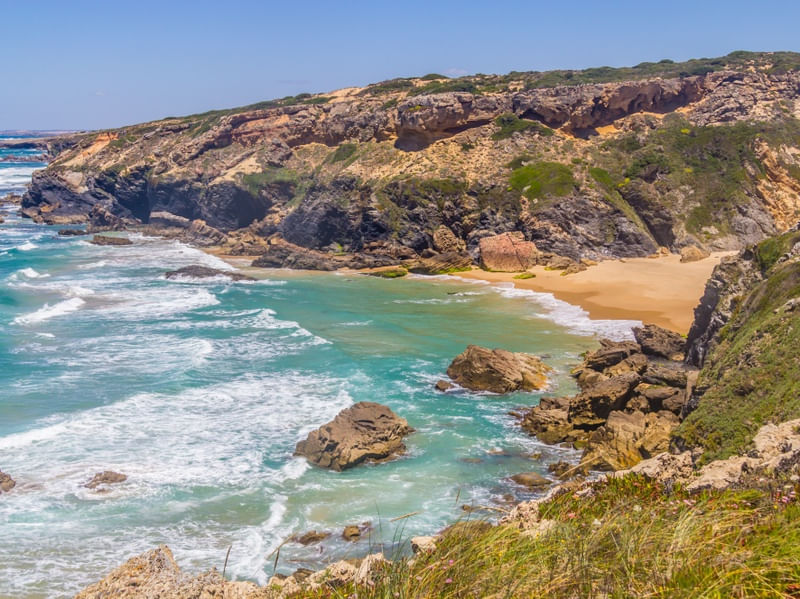 PRAIA ENTRE FALÉSIAS COM VEGETAÇÃO E ÁGUAS VERDES