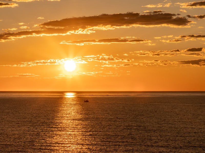 NASCER DO SOL NO OCEANO COM NUVENS E PEQUENO BARCO PESQUEIRO