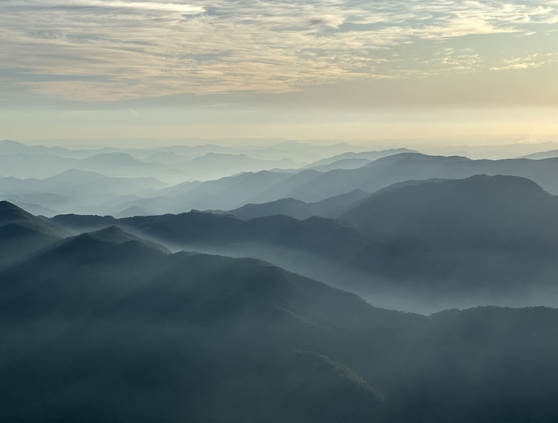 RAIOS DE SOL E NÉVOA SOBRE SILHUETA DE MONTANHAS DE UM PICO