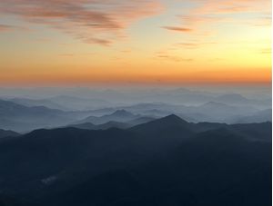 UM PÔR DO SOL E AS NÉVOAS NUMA SILHUETA DE MONTANHAS NUM PICO