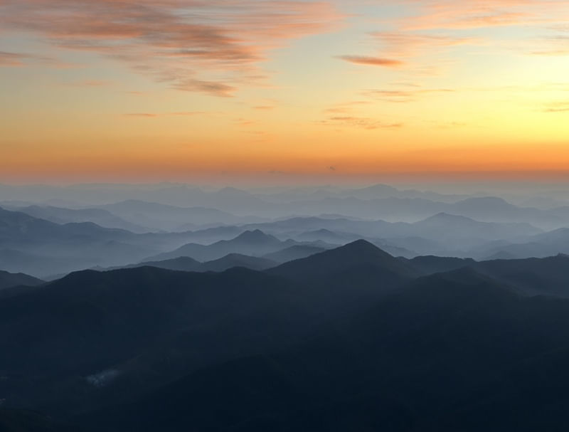 UM PÔR DO SOL E AS NÉVOAS NUMA SILHUETA DE MONTANHAS NUM PICO