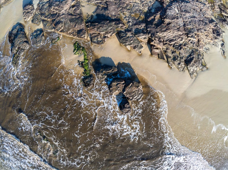 FOTO AÉREA DE ROCHAS, AREIA E ONDAS NA PRAIA DE TORRES